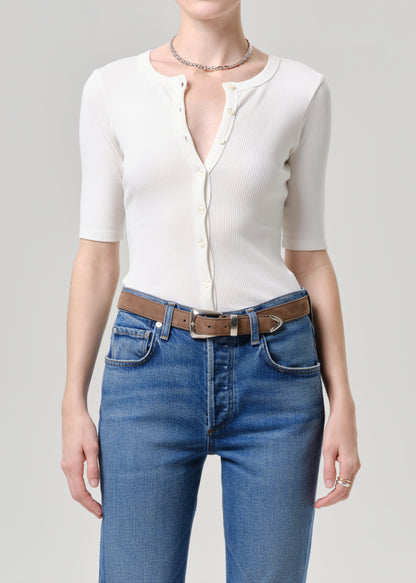 Person wearing a white ribbed knit top and blue jeans on a grey background