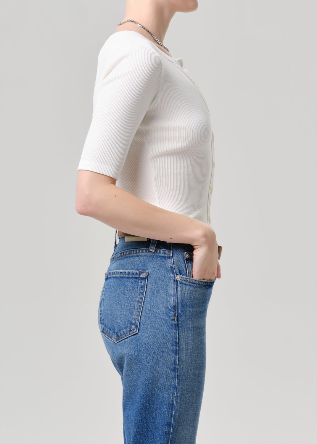 Person wearing a white top and blue jeans on a light grey background