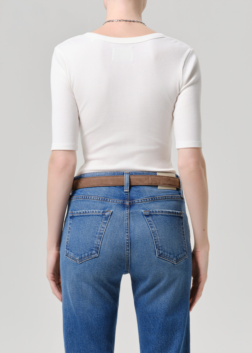 Person wearing a white top and blue jeans with a brown belt on a grey background