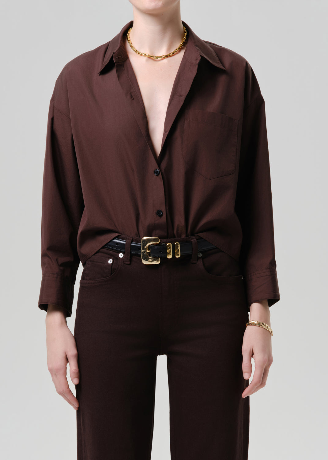 Person wearing a brown button-up shirt and pants with a belt on a grey background