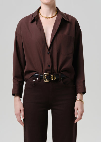 Person wearing a brown button-up shirt and pants with a belt on a grey background