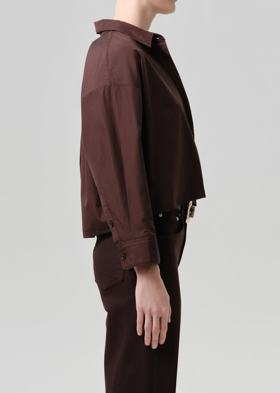 Person wearing a brown jacket and pants on a grey background