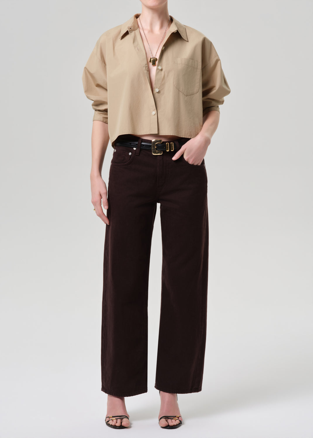 Person wearing a beige shirt and dark pants on a grey background