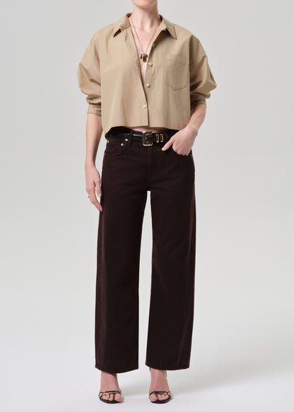 Person wearing a beige shirt and dark pants on a grey background