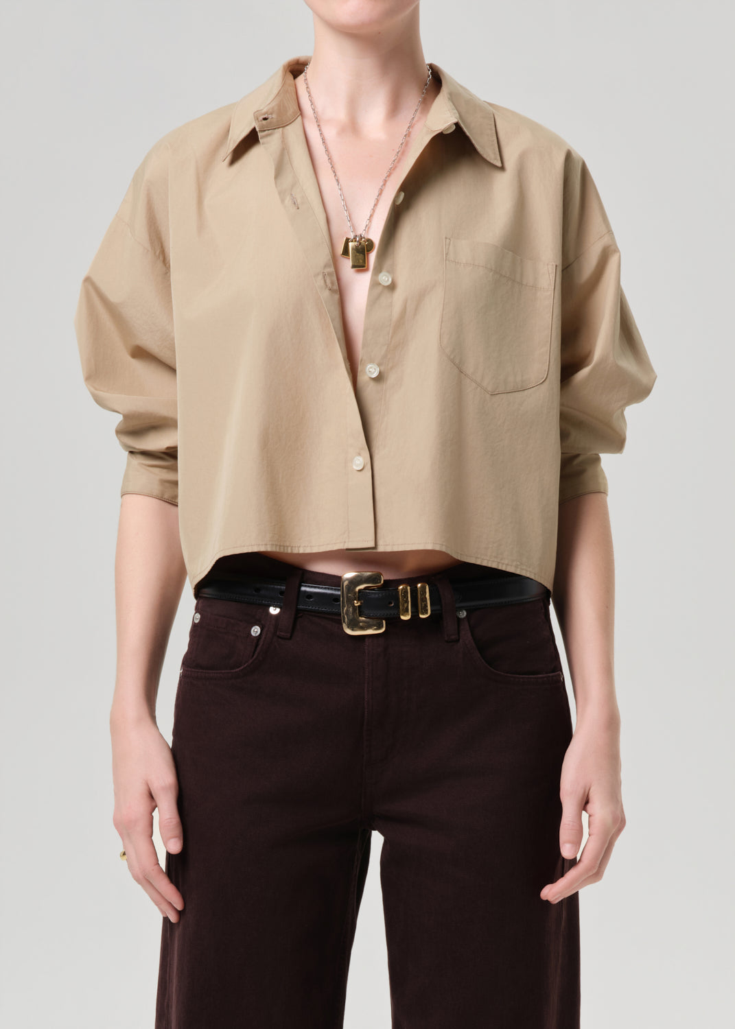 Person wearing a beige shirt and dark pants on a grey background