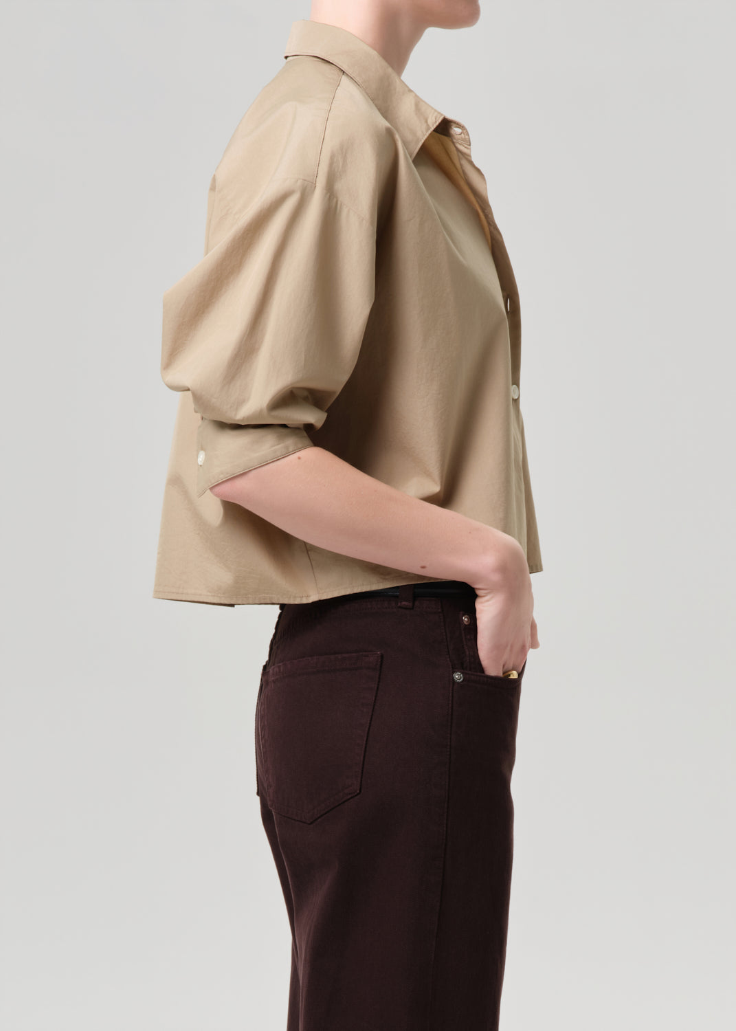 Person wearing a beige shirt and dark pants on a grey background
