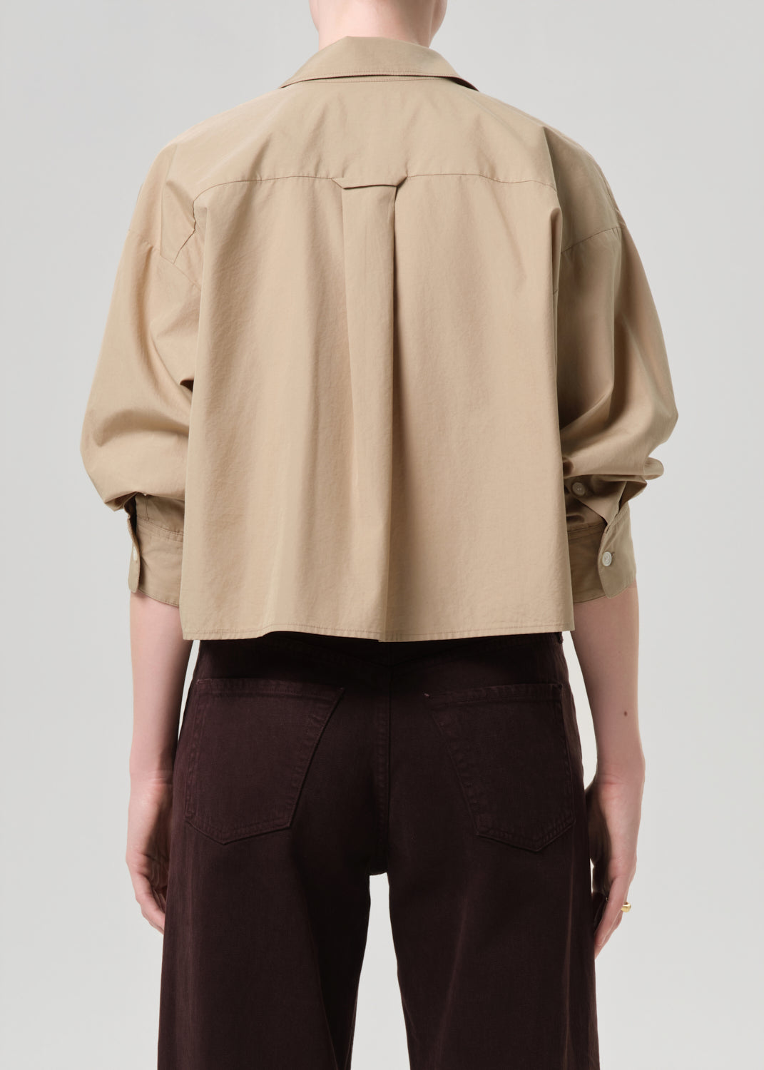Person wearing a beige jacket and dark pants on a grey background