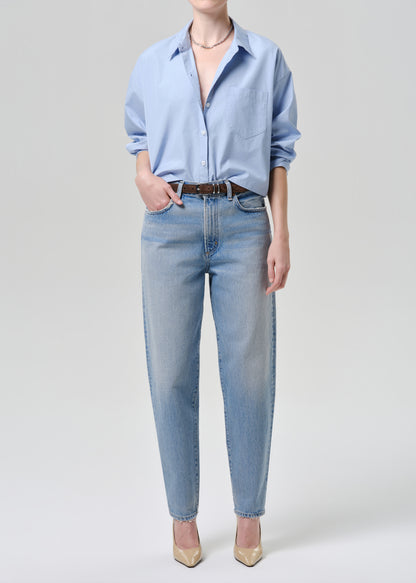 Person wearing a light blue shirt and jeans on a grey background