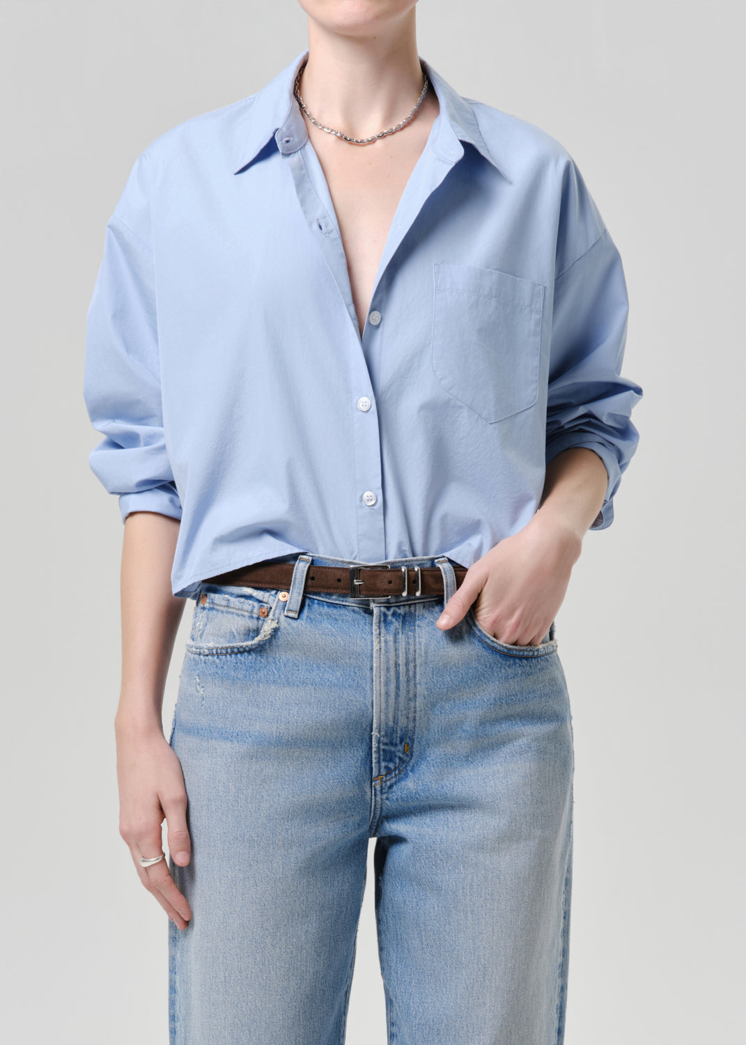 Person wearing a light blue button-up shirt and jeans on a grey background