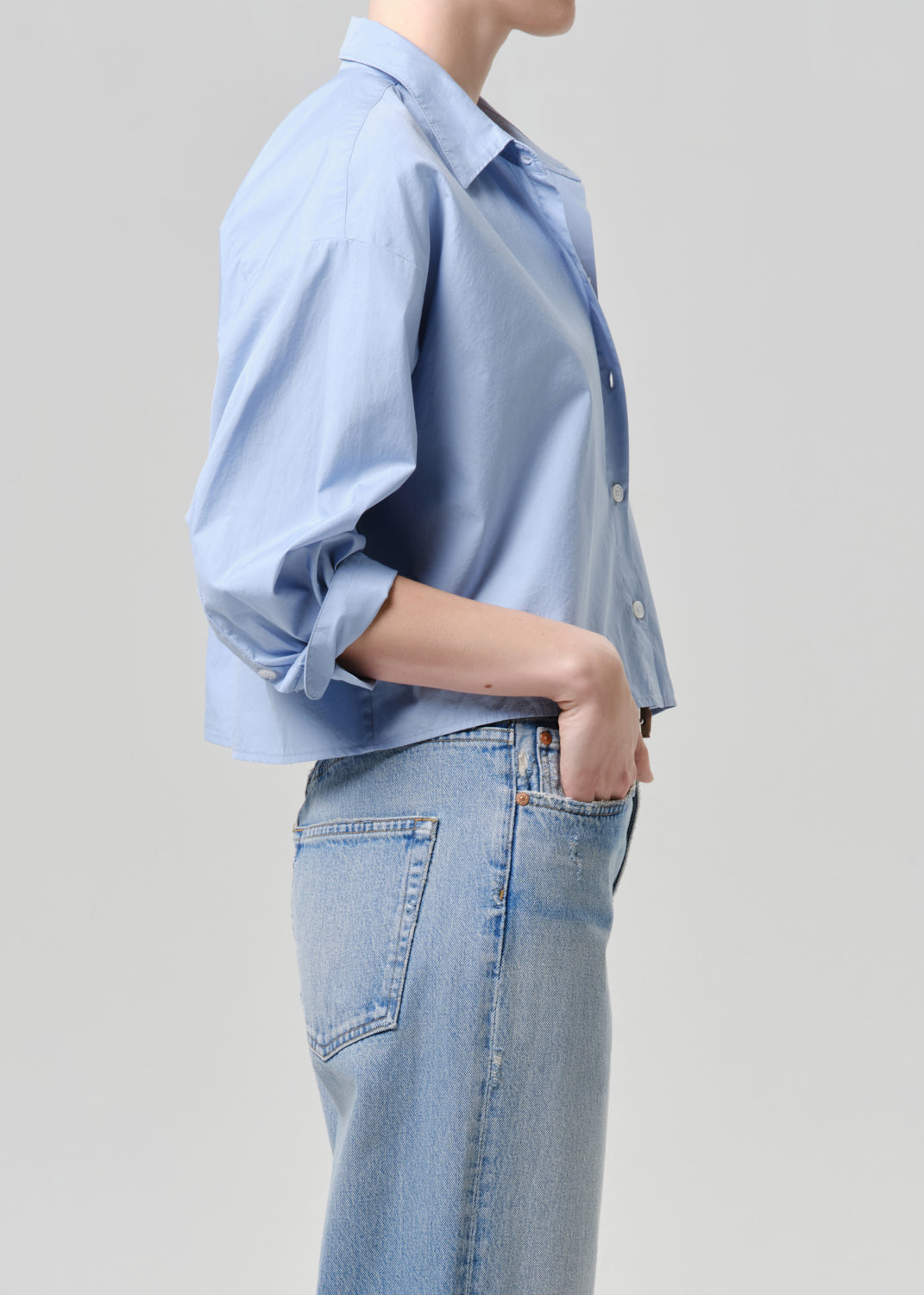 Person wearing a light blue shirt and jeans on a grey background