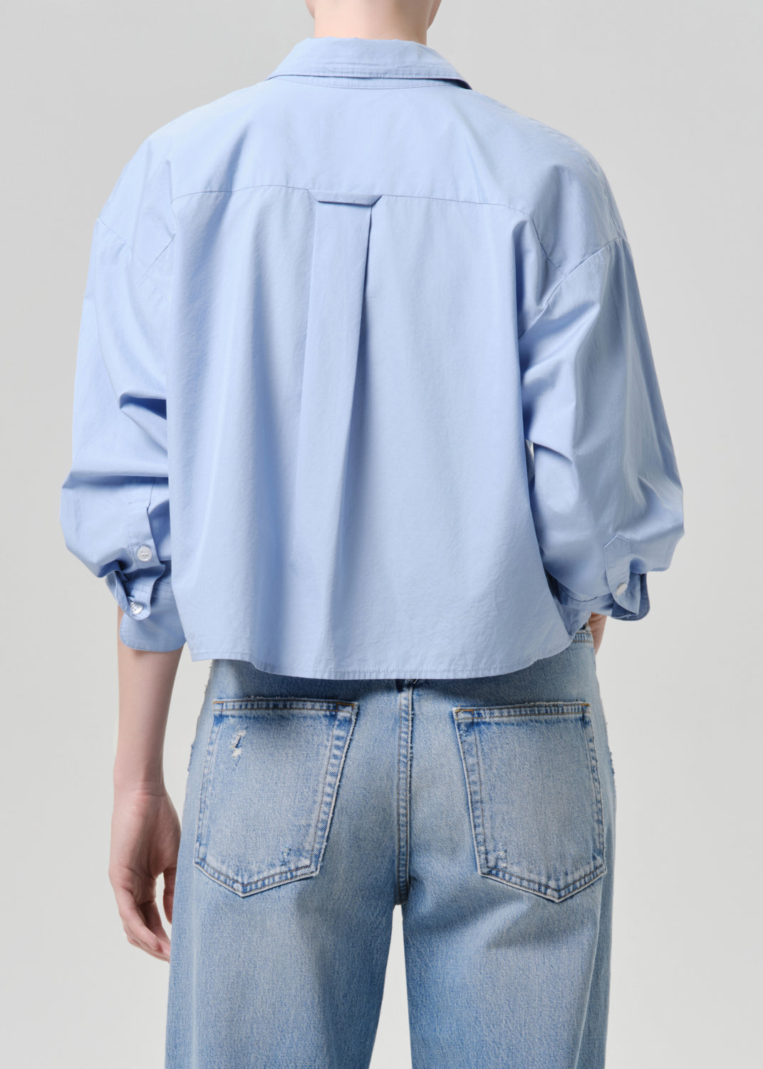 Person wearing a light blue shirt and jeans against a grey background