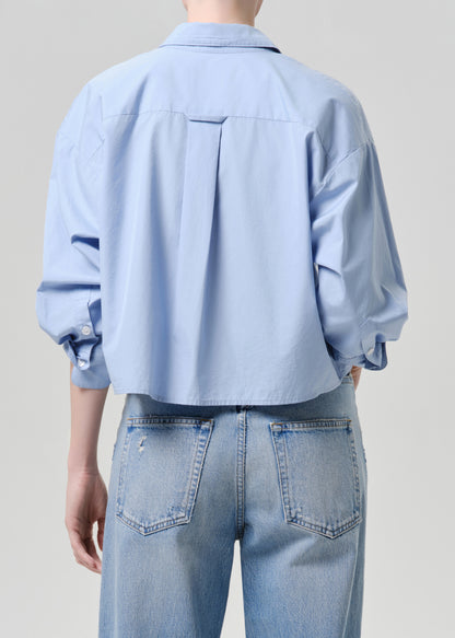 Person wearing a light blue shirt and jeans against a grey background