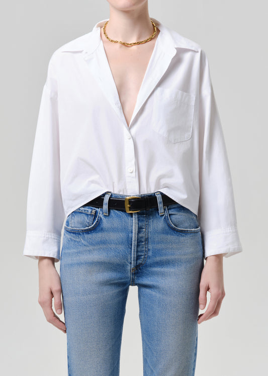 Person wearing a white button-up shirt and blue jeans on a grey background