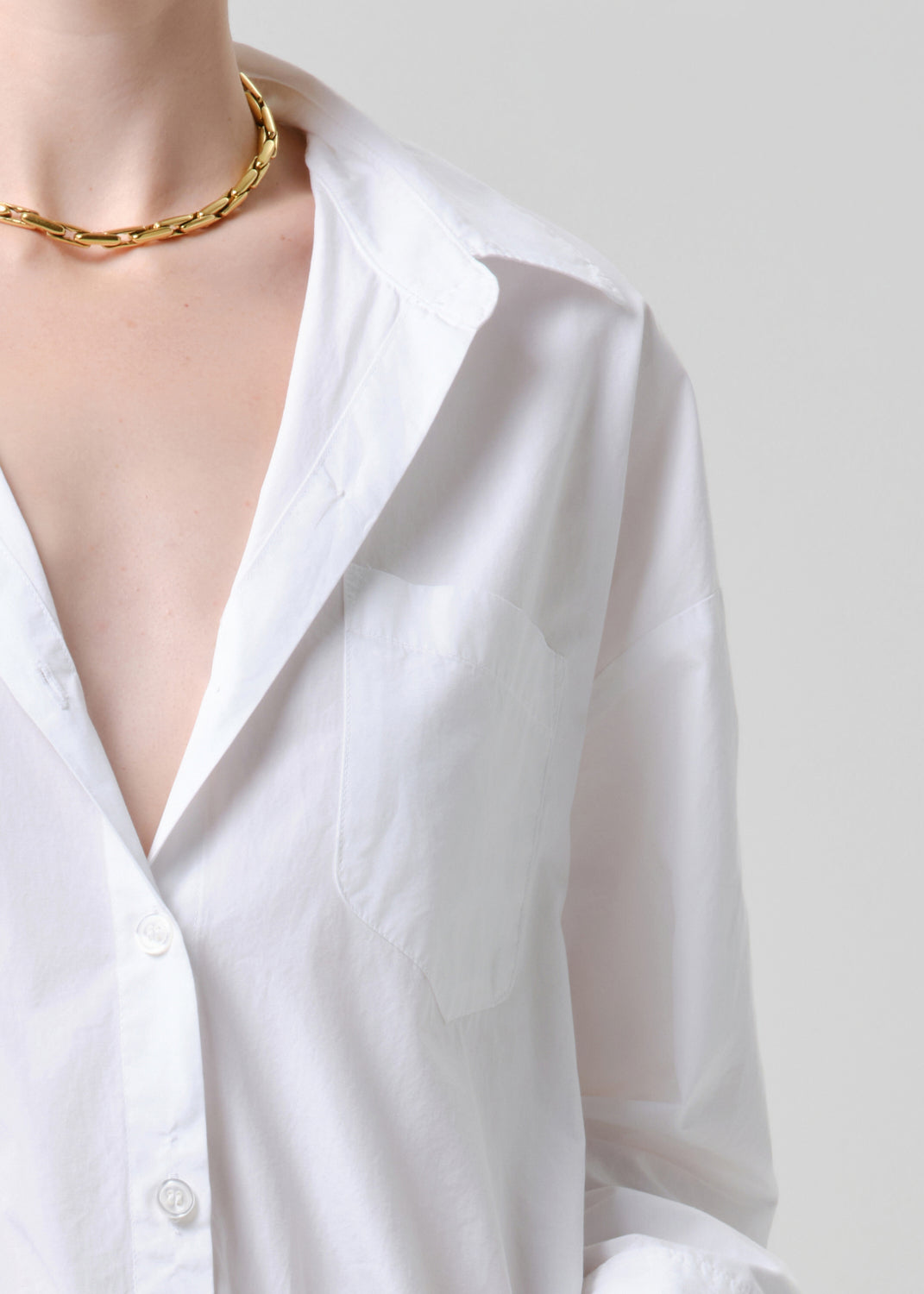 White shirt with a gold chain necklace on a grey background