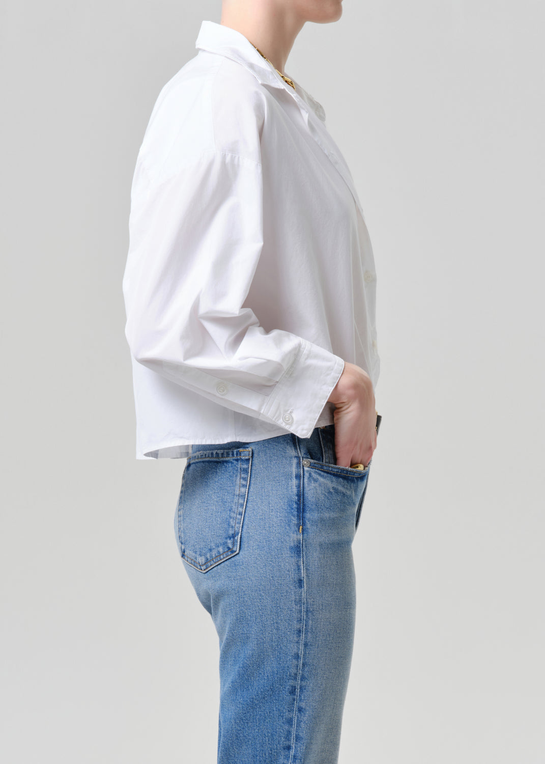 Person wearing a white shirt and blue jeans against a grey background