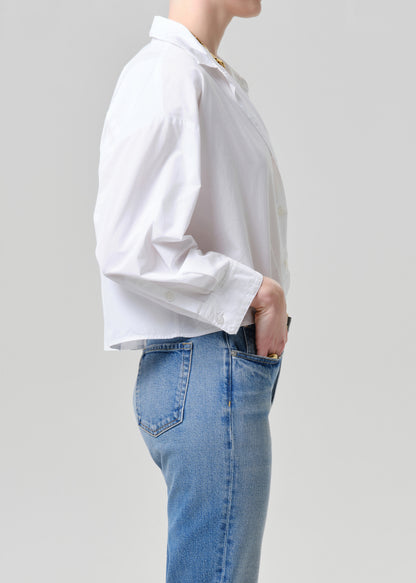 Person wearing a white shirt and blue jeans against a grey background