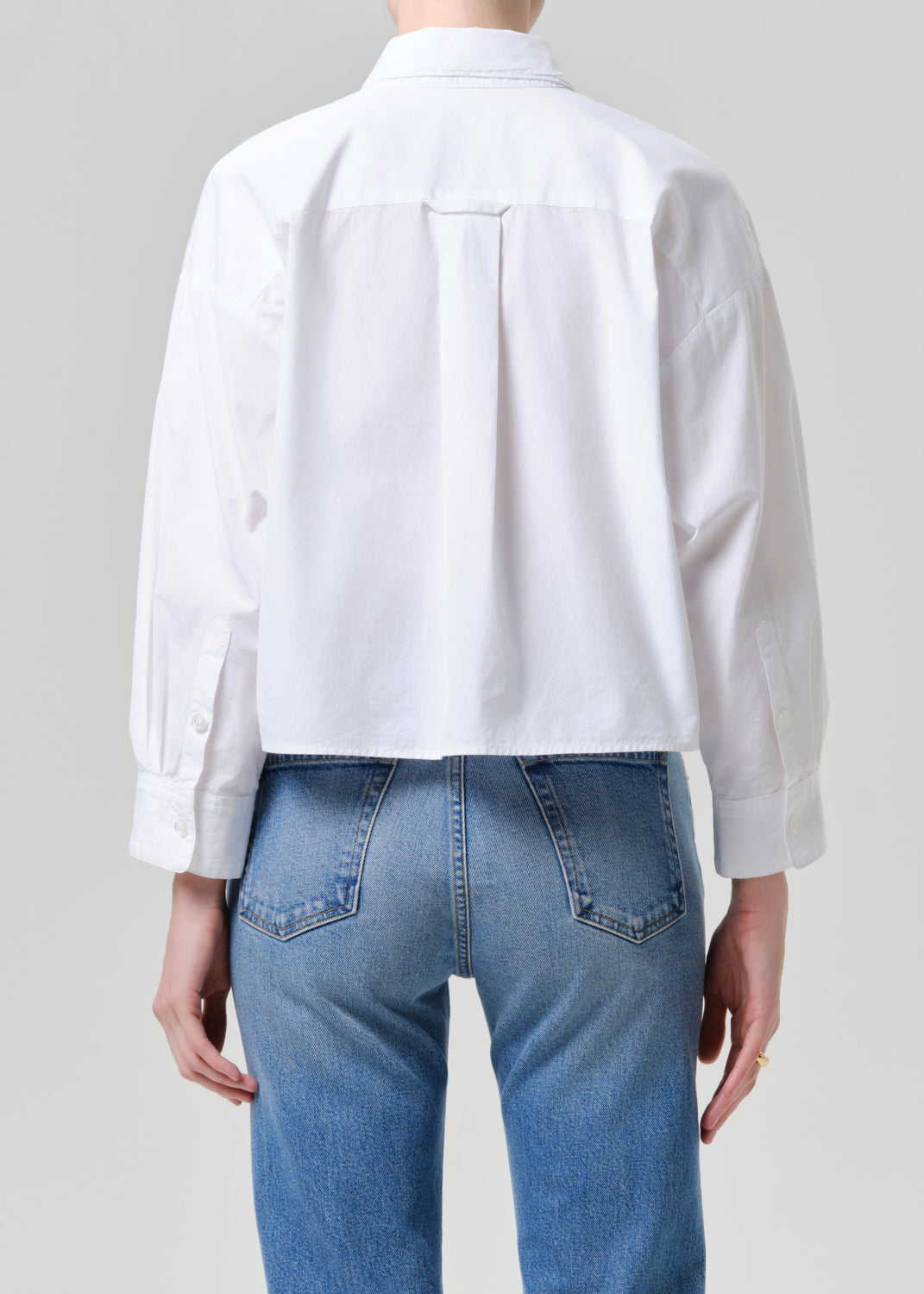 Person wearing a white shirt and blue jeans on a grey background
