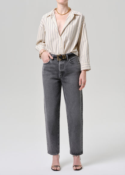 Person wearing a striped shirt and gray jeans on a grey background