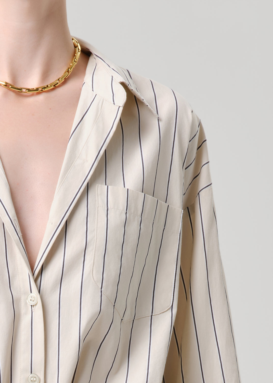Close-up of a person wearing a beige striped shirt with a gold necklace on a grey background