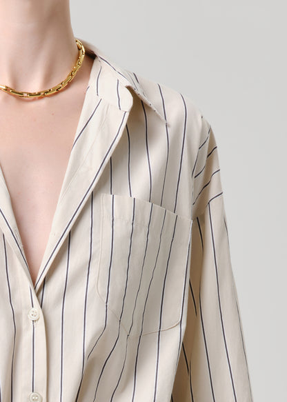 Close-up of a person wearing a beige striped shirt with a gold necklace on a grey background