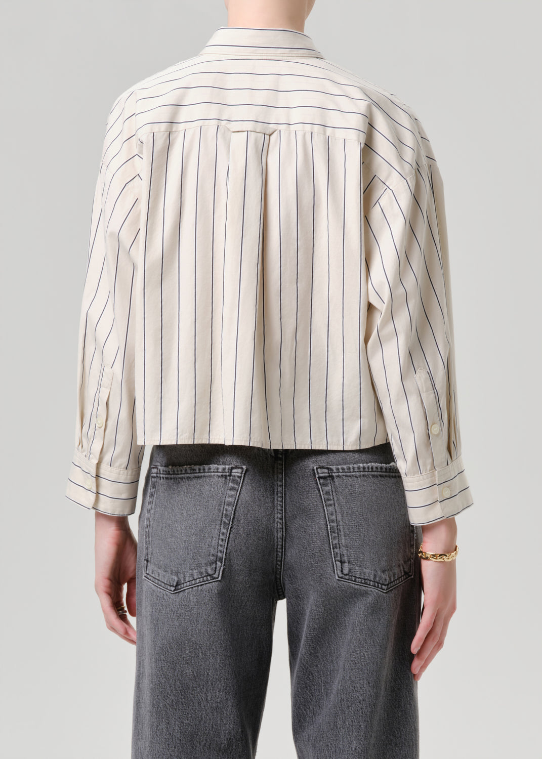 Person wearing a striped shirt and dark jeans on a grey background