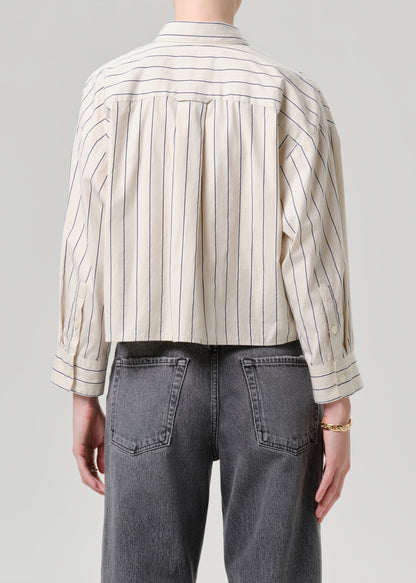 Person wearing a striped shirt and dark jeans on a grey background
