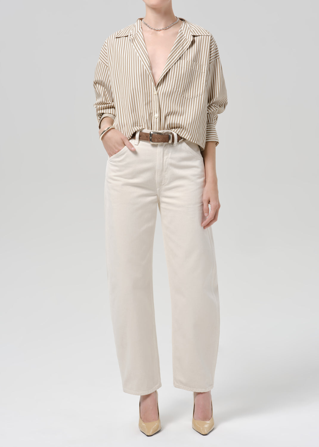 Person wearing a beige striped long sleeve shirt tucked into white denim pants on a grey background.