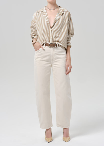 Person wearing a beige striped long sleeve shirt tucked into white denim pants on a grey background.