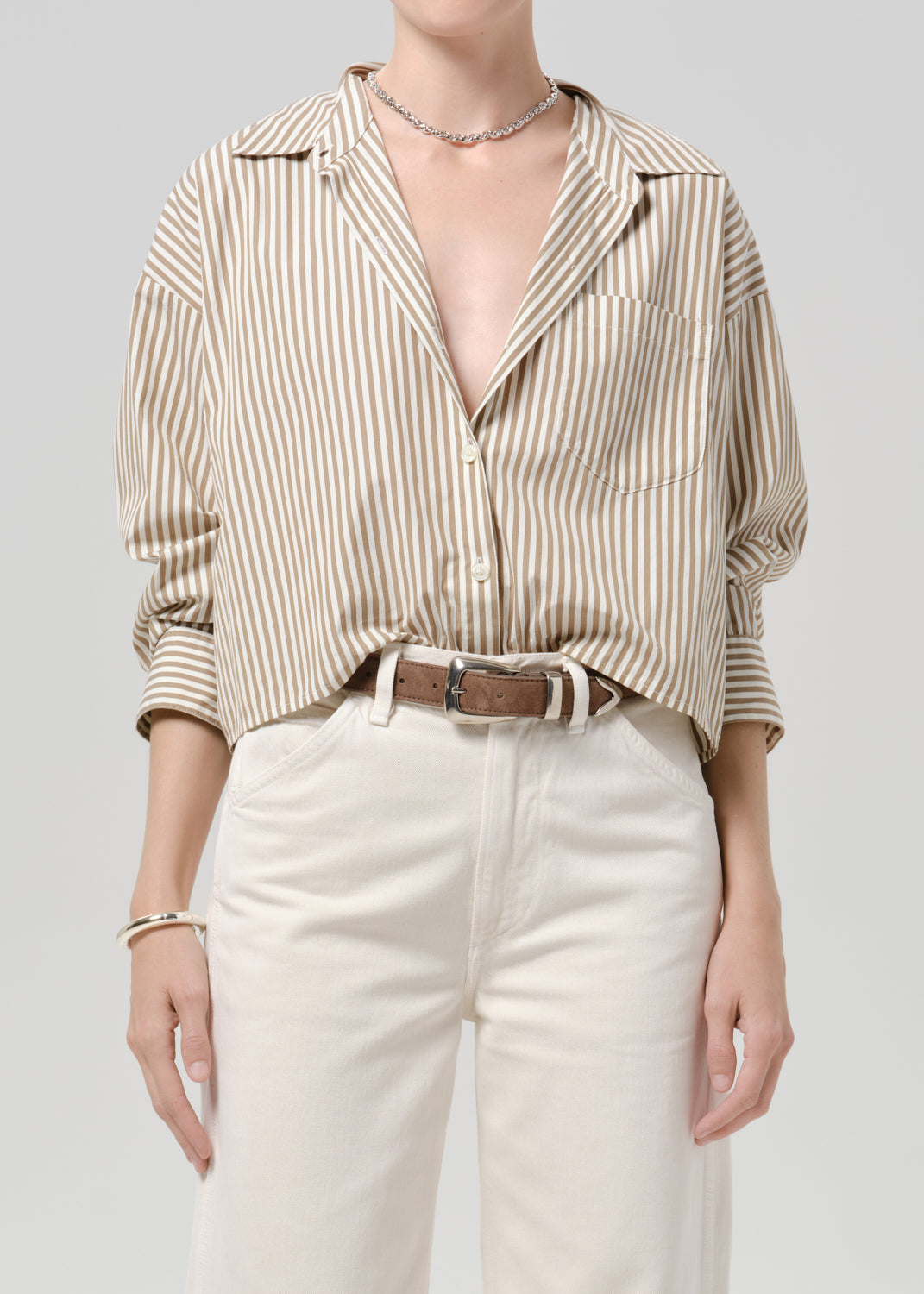Person wearing a beige and white striped button-up shirt with white pants on a grey background