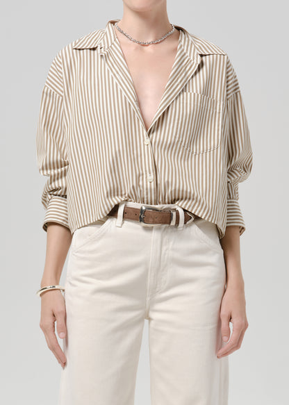 Person wearing a beige and white striped button-up shirt with white pants on a grey background