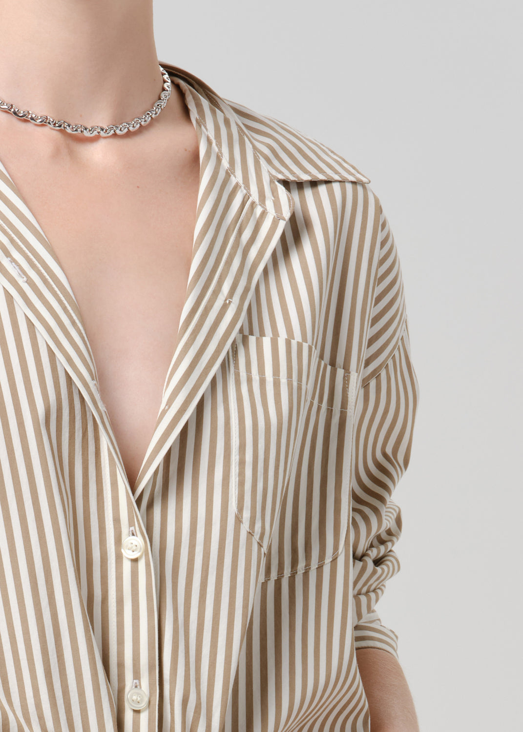Person wearing a beige and white striped woven shirt on a grey background.