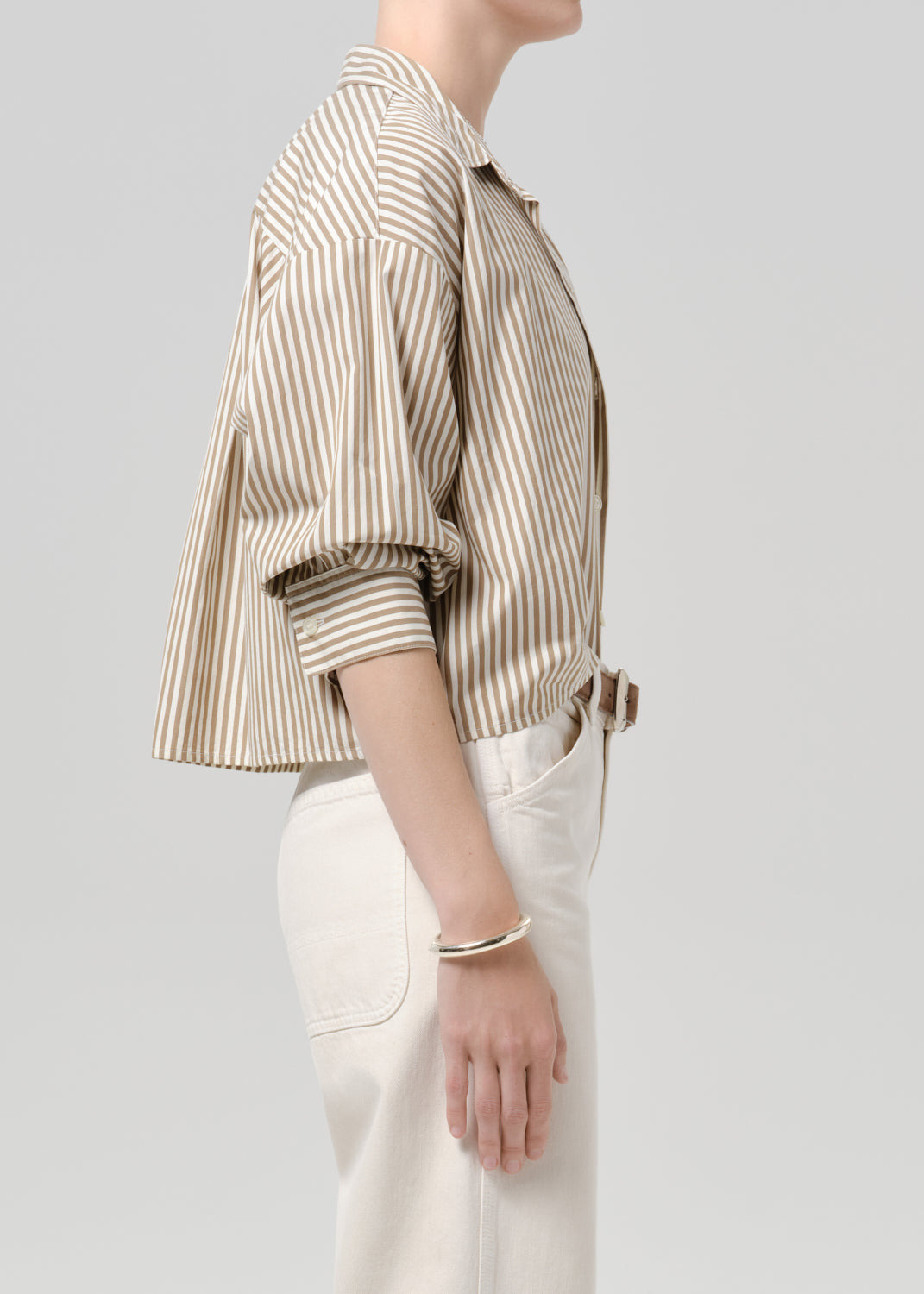 Person wearing a striped button-front shirt in beige and ivory paired with white pants on a grey background.