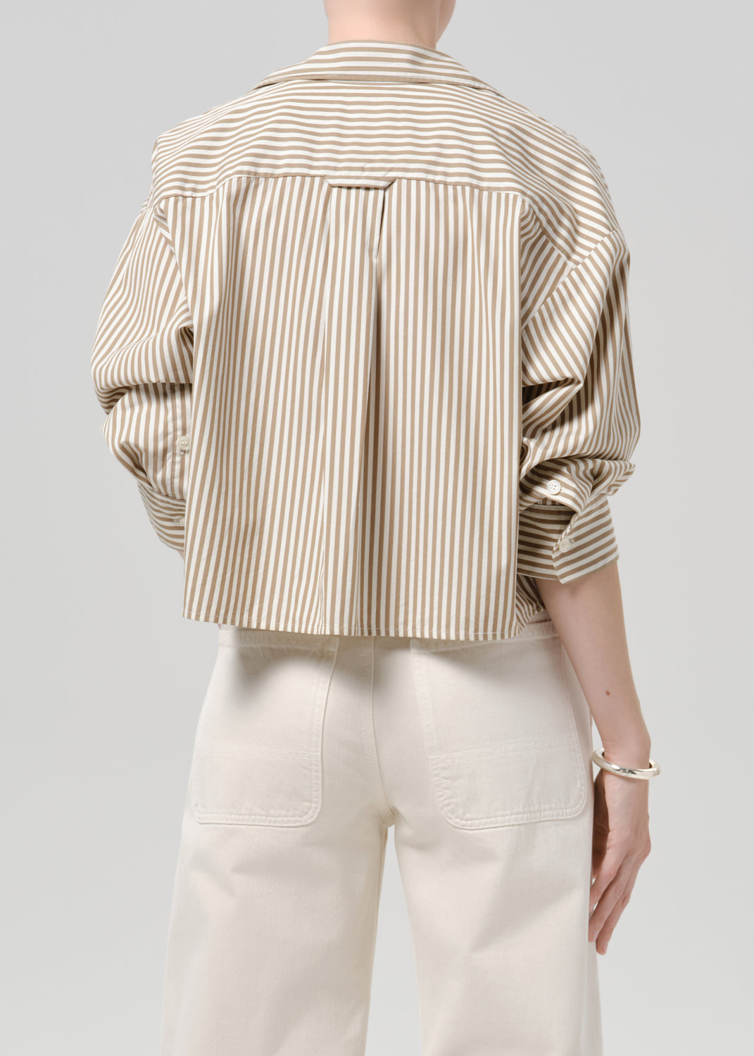 Person wearing a relaxed beige and ivory striped shirt with white jeans on a grey background