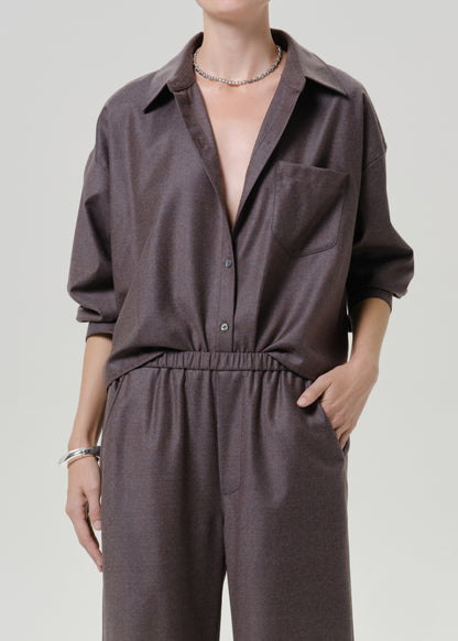 Woman wearing a dark brown short sleeve button-up shirt with matching dark brown wide leg pants on a grey background.