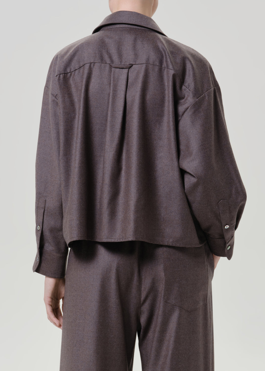 Woman wearing a dark brown short sleeve button-up shirt with matching dark brown wide leg pants viewed from the back on a grey background.
