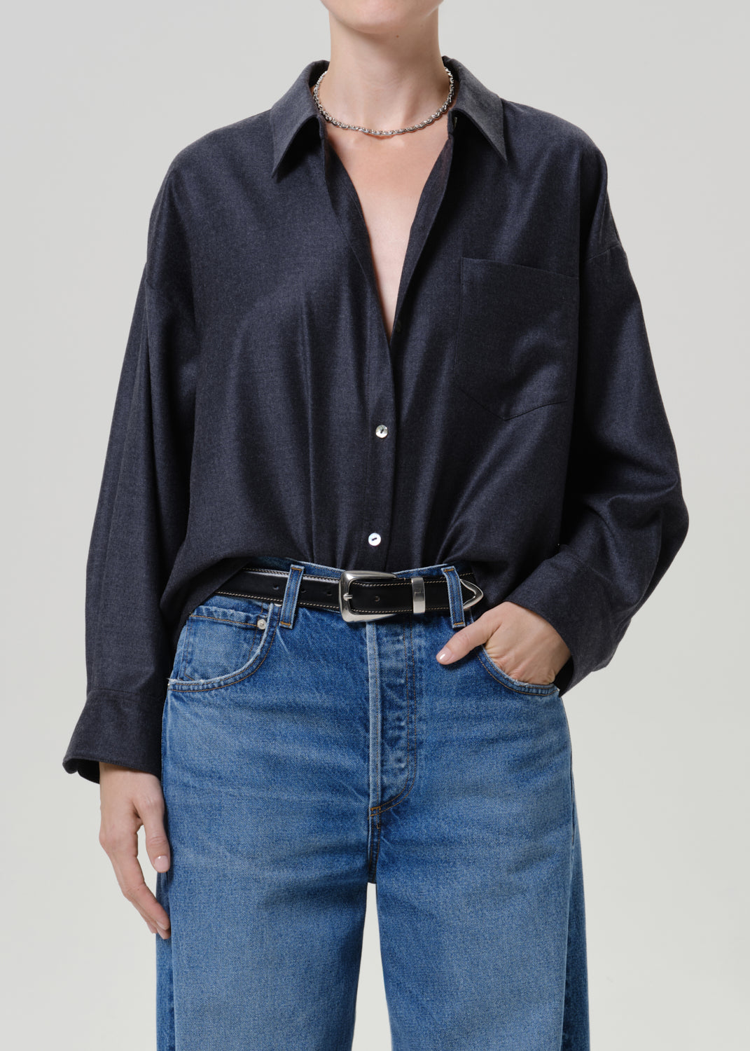 Woman wearing a dark navy button-up shirt with medium blue jeans on a grey background.