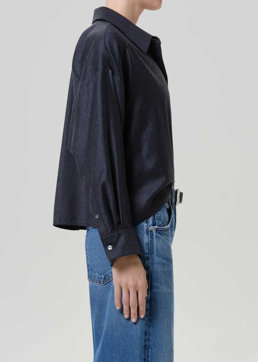 Woman wearing a dark navy button-up shirt with medium blue jeans viewed from the side on a grey background.
