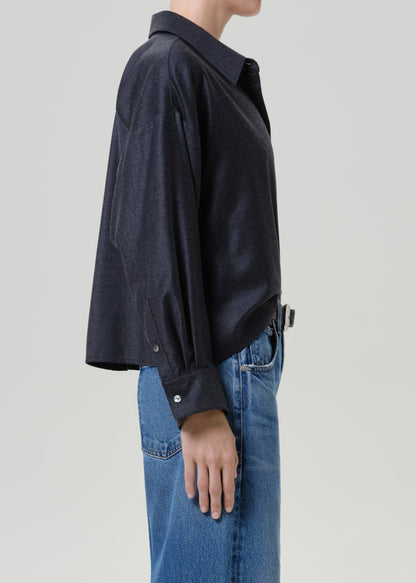Woman wearing a dark navy button-up shirt with medium blue jeans viewed from the side on a grey background.