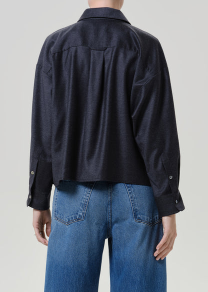 Woman wearing a dark navy button-up shirt with medium blue jeans viewed from the back on a grey background.