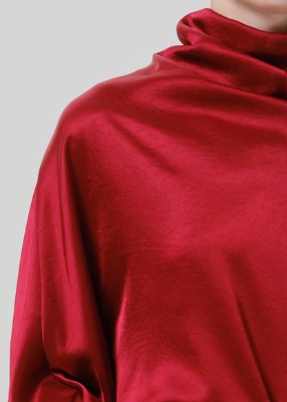 Close-up of a red satin draped neck top on a grey background.