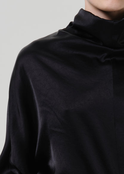 Close-up of a black satin draped neck top on a grey background.