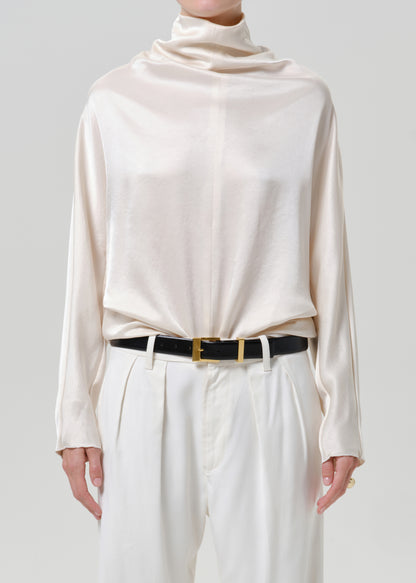 Woman wearing an ivory satin draped neck top with white wide leg pants on a grey background.