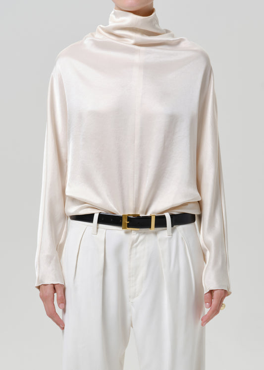 Woman wearing an ivory satin draped neck top with white wide leg pants on a grey background.