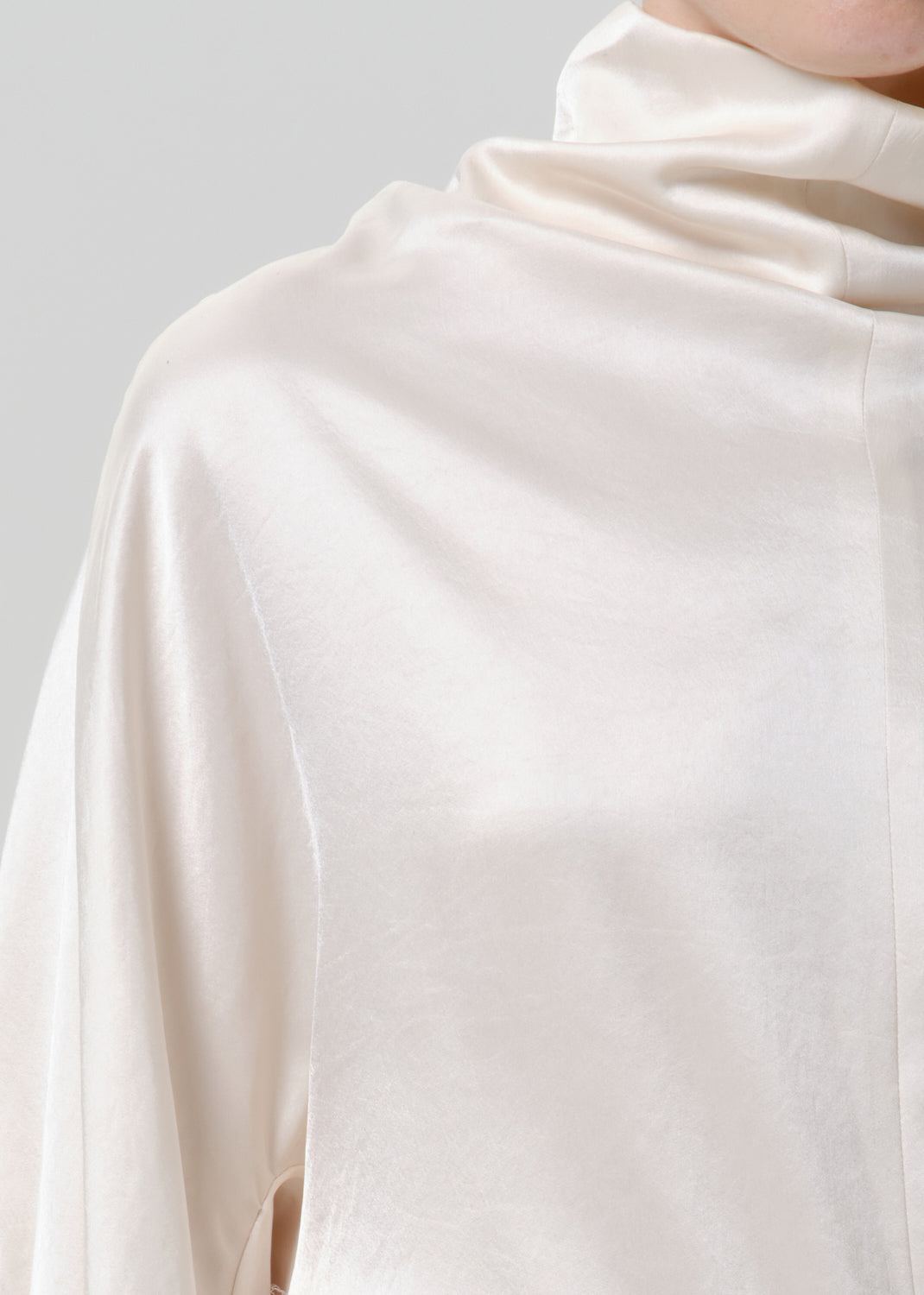 Close-up of an ivory satin draped neck top on a grey background.