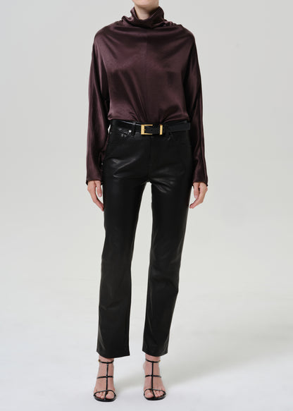 Woman wearing a dark brown satin draped neck top with black leather pants on a grey background.