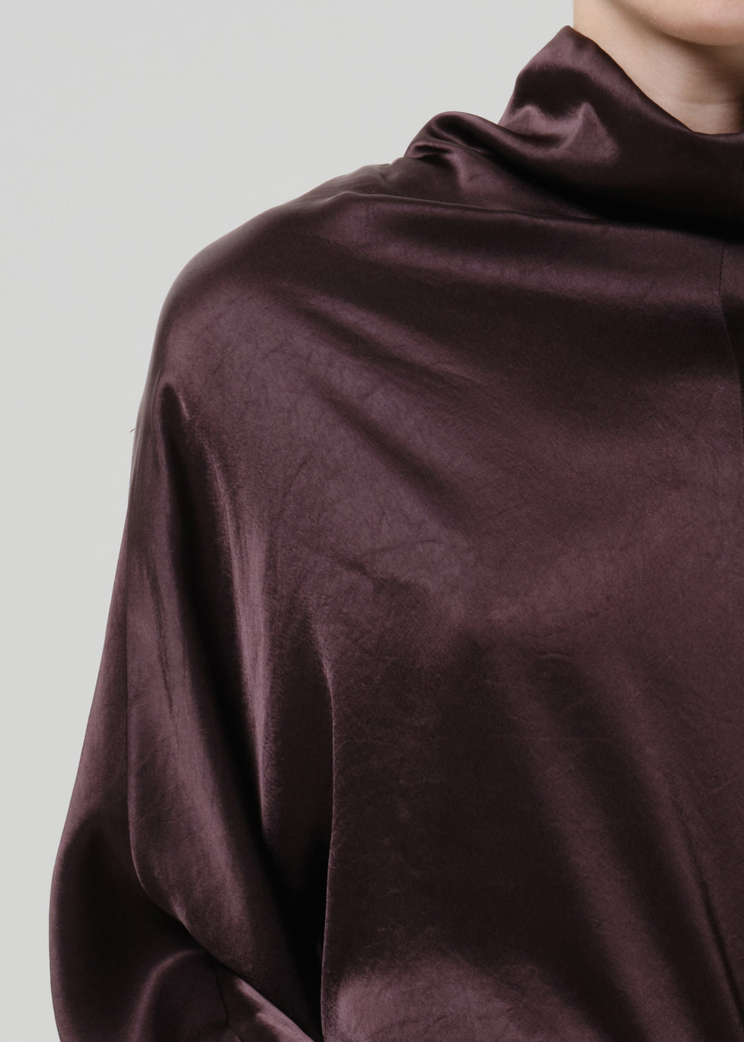 Close-up of a dark brown satin draped neck top on a grey background.