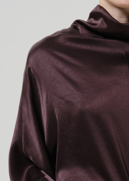 Close-up of a dark brown satin draped neck top on a grey background.