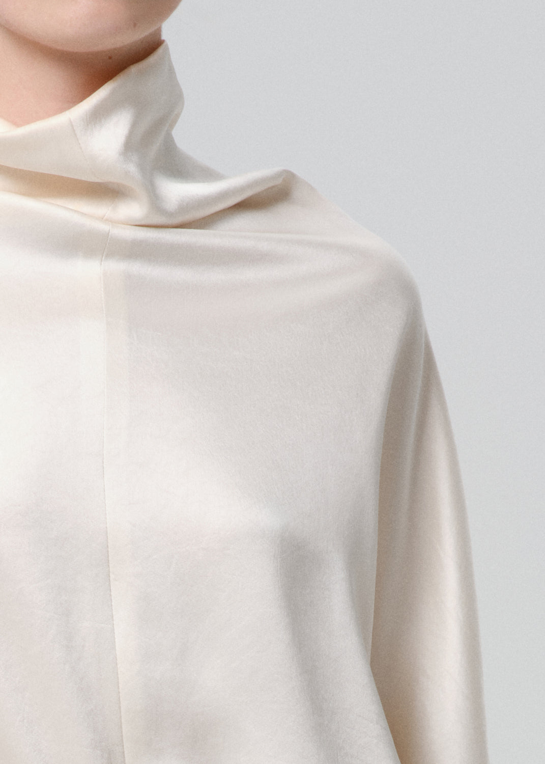 Close-up of an ivory draped cowl neck blouse on a grey background