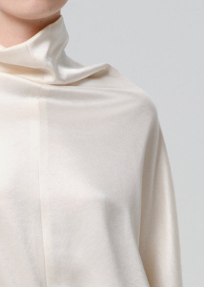 Close-up of an ivory draped cowl neck blouse on a grey background