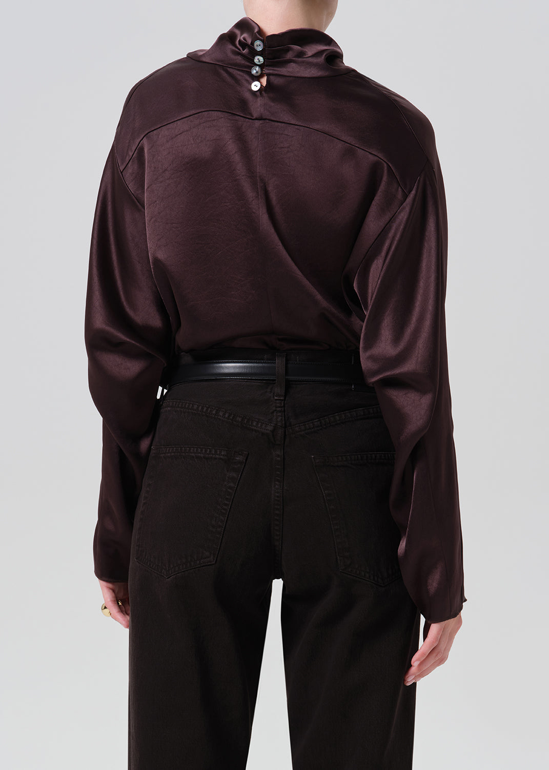 A person shown from the back wearing a dark plum satin long-sleeve top with decorative buttons at the collar and black pants, against a grey background.